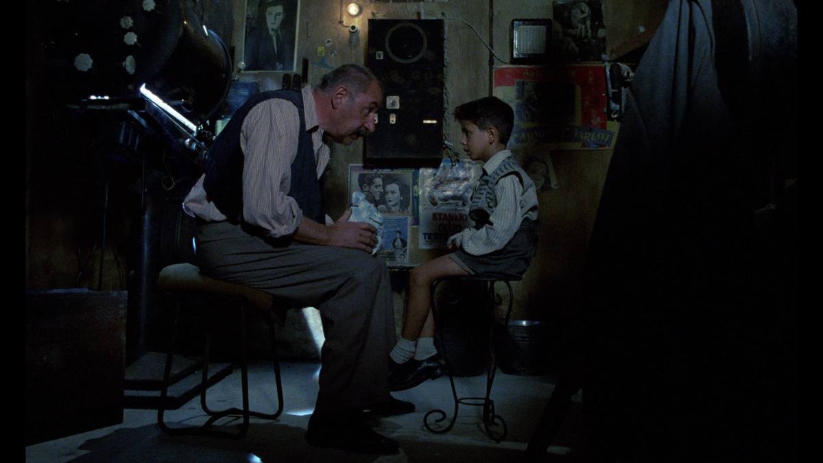 Il proiezionista Alfredo (Philippe Noiret) seduto di fronte al suo giovane protetto Salvatore Di Vita (Salvatore Cascio) al Cinema Paradiso.