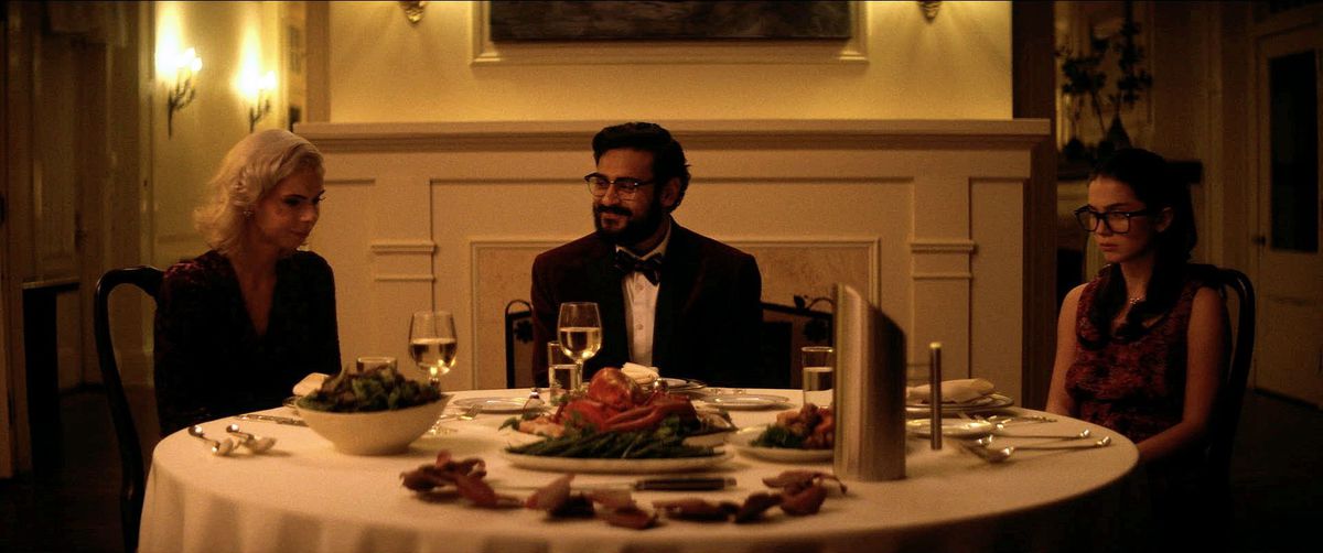 Tre persone siedono a un piccolo tavolo rotondo con un assortimento di cibo e decorazioni in luci al neon.