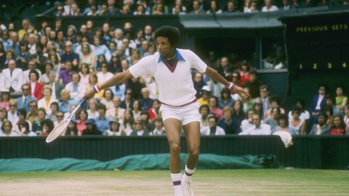 Arthur Ashe colpisce un rovescio su un campo da tennis mentre la folla guarda.
