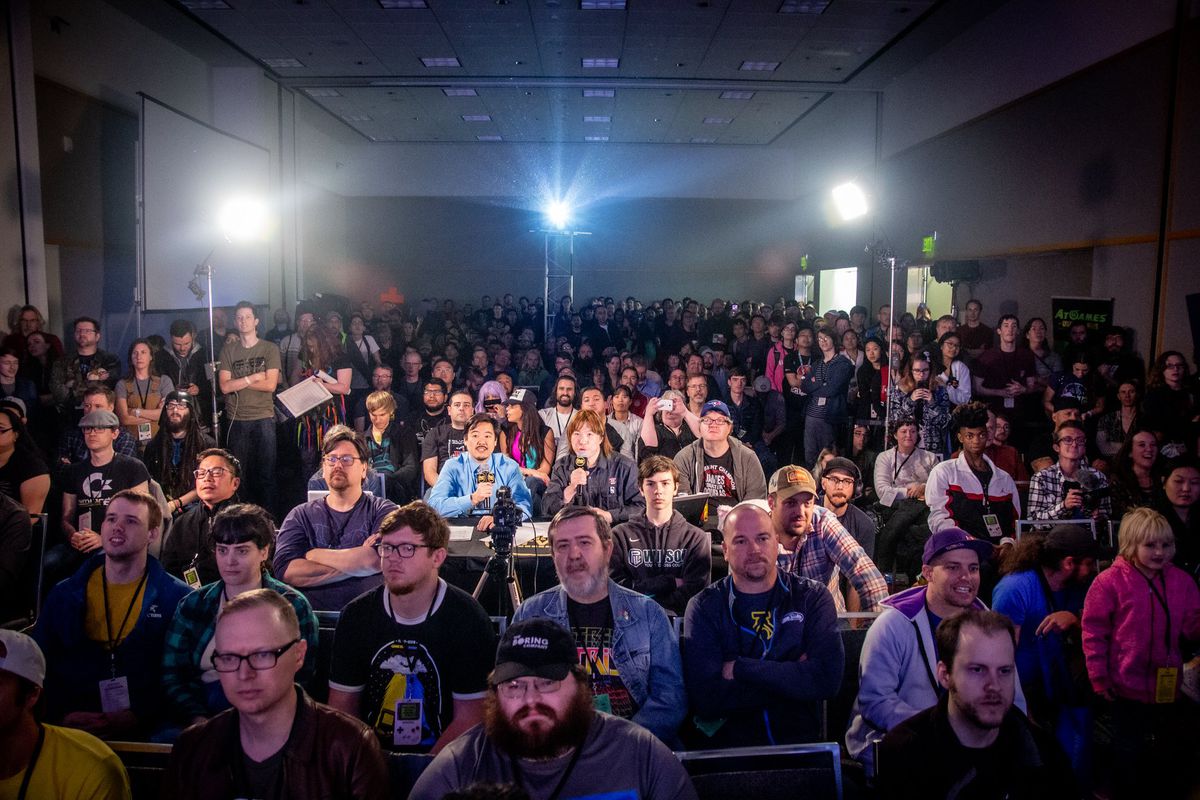 Una folla di oltre 100 spettatori che assiste al CTWC 2019. I commentatori James Chen e Chris Tang siedono a un tavolo ben illuminato nel mezzo.