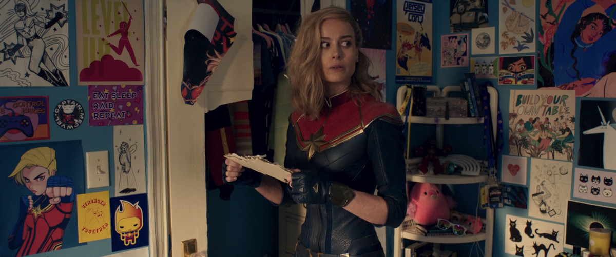 Carol Danvers (Brie Larson) sembra confusa nella camera da letto di Kamala Khan, che è decorata con cimeli di Carol Danvers e fanart in Ms. Marvel.