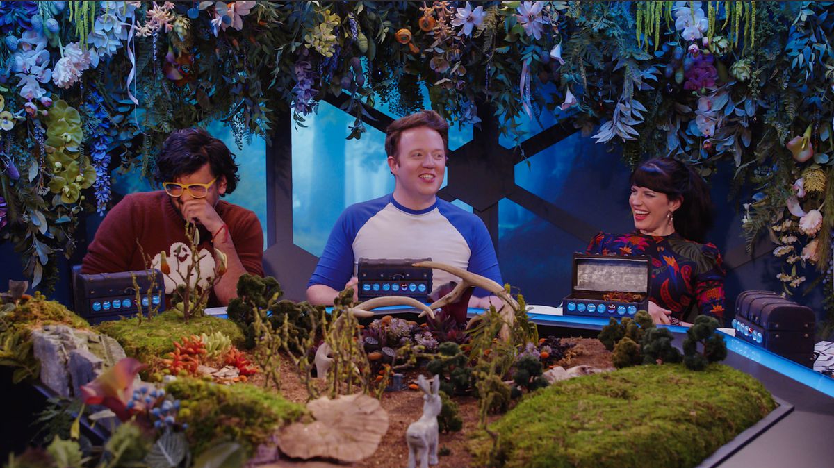 Tre giocatori circondati da fiori e ghirlande giocano a D&D.