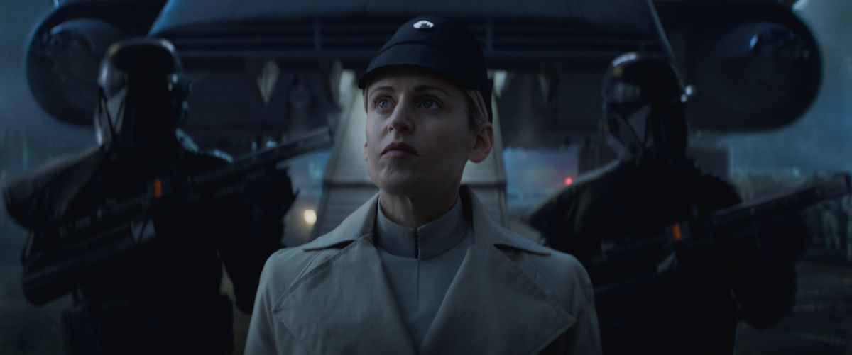 Dedra Meero in piedi davanti a una rampa di una nave che guarda in alto, con due guardie imperiali dietro di lei