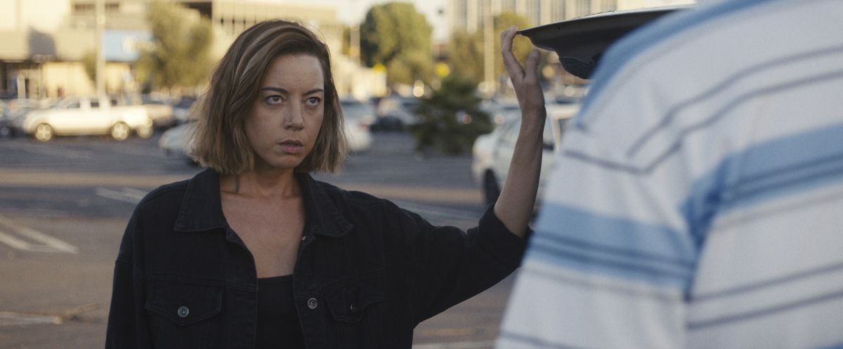 Aubrey Plaza mentre Emily è in piedi accanto al bagagliaio della sua auto, fissando un potenziale acquirente in Emily the Criminal