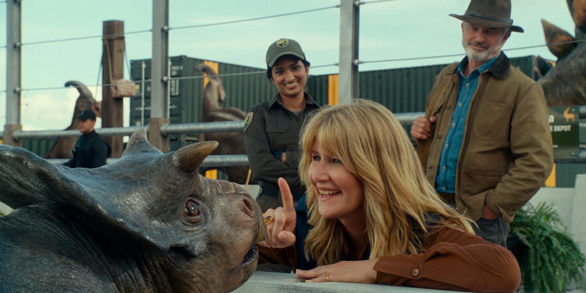 La dottoressa Ellie Sattler (Laura Dern) allunga un dito verso un piccolo Nasutoceratops in un modo che fa sembrare che stia per ficcarselo sul naso, mentre il dottor Alan Grant (Sam Neill) osserva in Jurassic World Dominion.