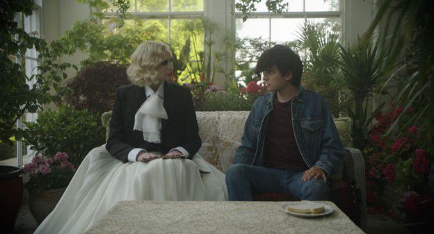 Gwendoline Christie, in un fluido bianco e nero, e Asa Butterfield in denim si guardano su un divano in Flux Gourmet.