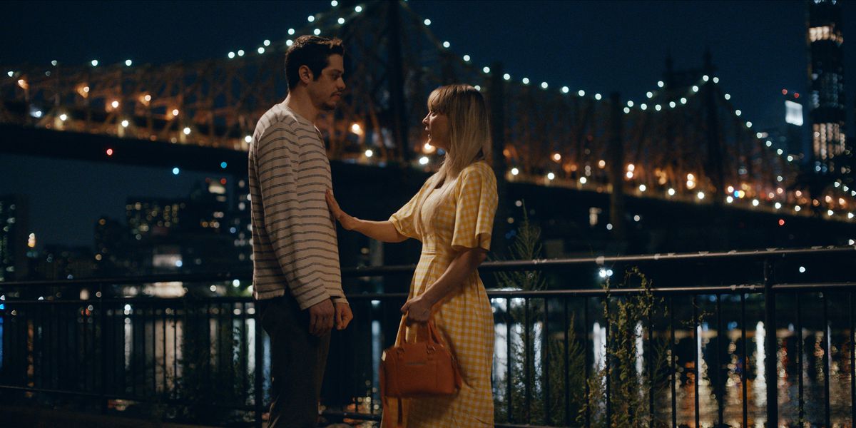 Pete Davidson e Kaley Cuoco in piedi accanto al ponte di Manhattan di notte.
