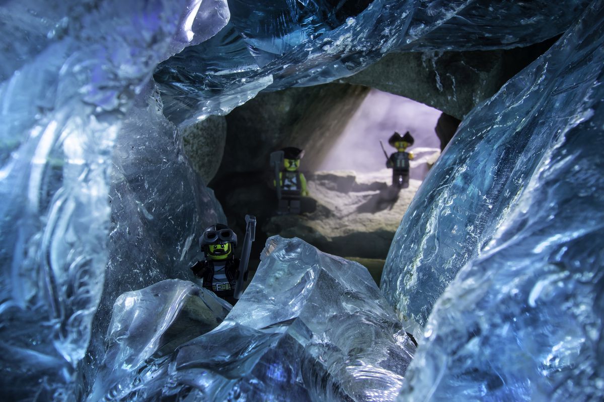 Una minifig Lego con barba e berretto da volo usa un piccone per scheggiare il ghiaccio mentre i suoi due amici pirati lo acclamano dalla bocca di una grotta