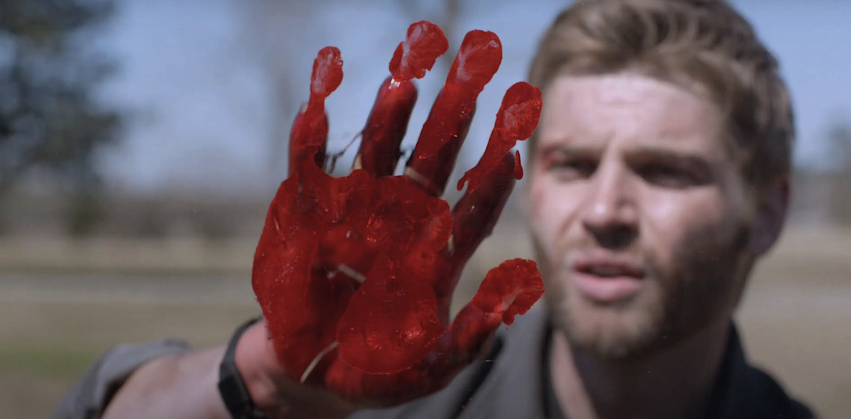 Un uomo bianco barbuto e dai capelli color sabbia fissa con stupore l'impronta rossa vivida e insanguinata che ha appena fatto su quella che sembra essere aria vuota nello show della CBS Under the Dome