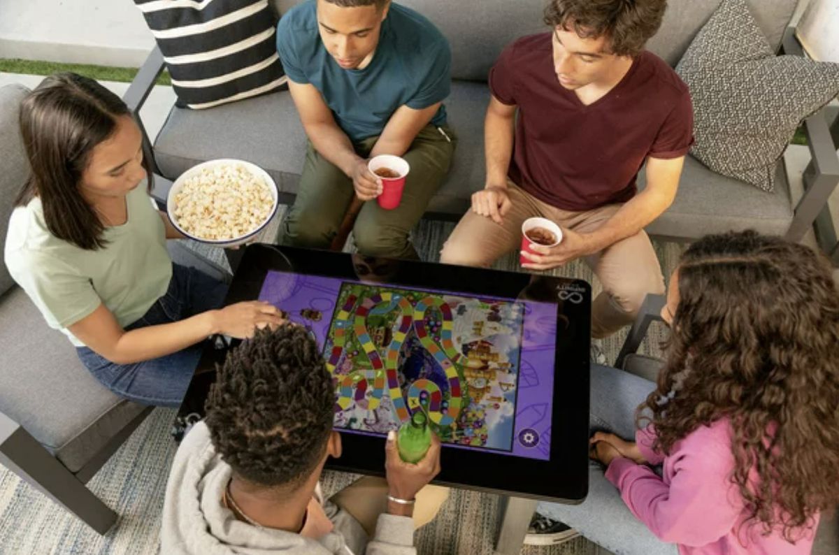Sei giocatori si siedono intorno a un tavolo digitale in soggiorno, giocando