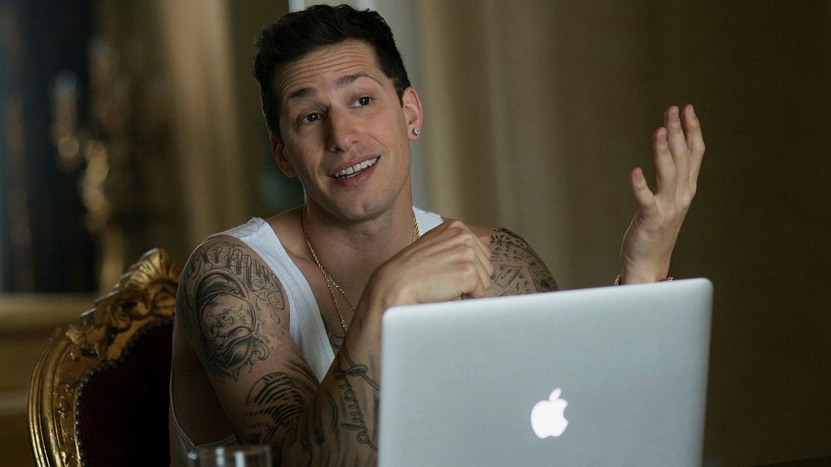 Un uomo con una felpa bianca seduto dietro un laptop Macintosh.