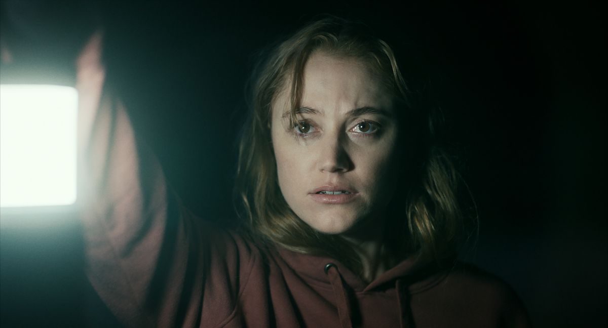 Una donna (Maika Monroe) con un maglione rosso regge una lanterna in una grotta buia.