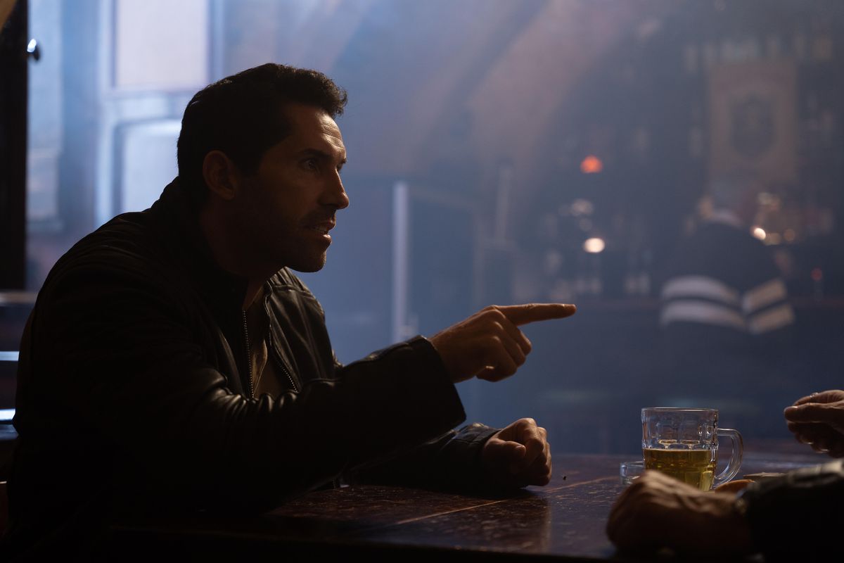 Scott Adkins punta il dito seduto al tavolo di un bar in Accident Man: Hitman's Holiday
