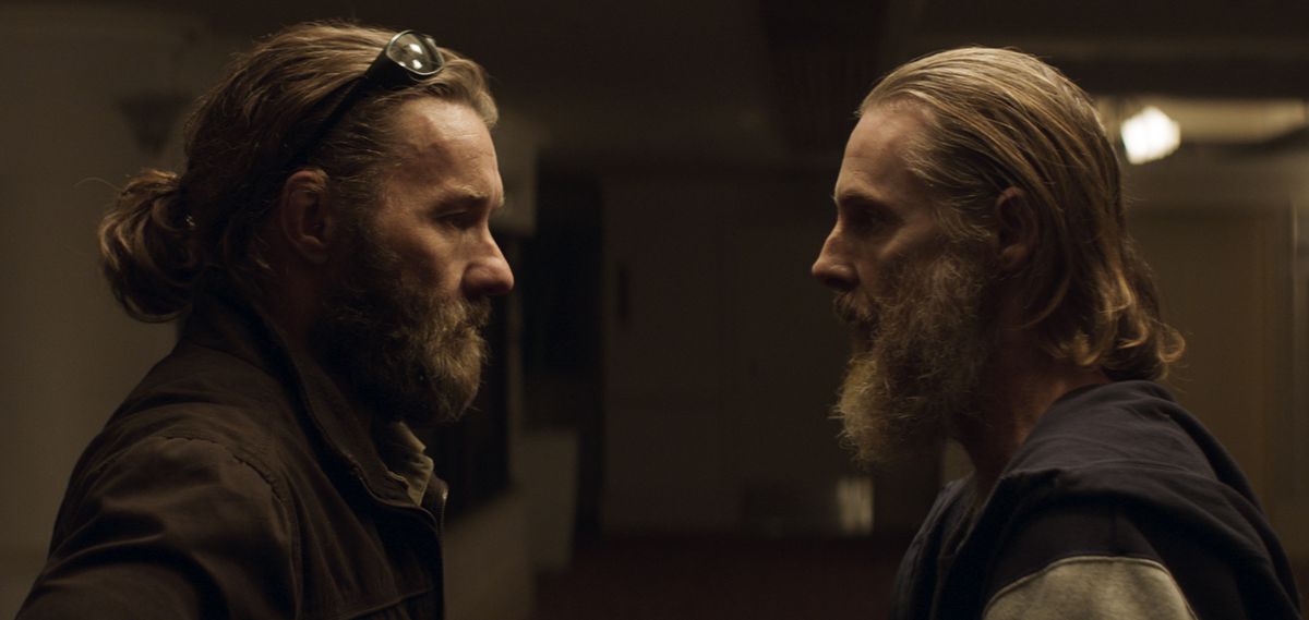 (LR) Un uomo barbuto (Joel Edgerton) con gli occhiali da sole in testa si alza e fissa severamente un altro uomo barbuto (Sean Harris) con una felpa con cappuccio.