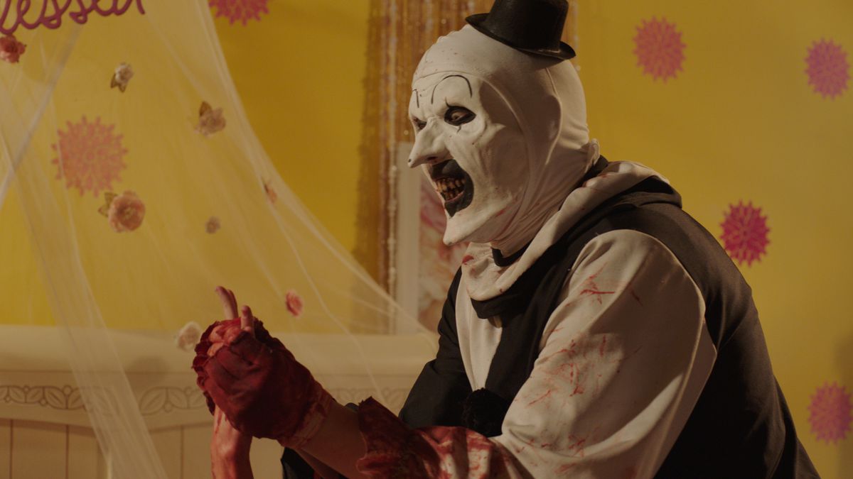 David Howard Thornton nei panni del mimo assassino Art the Clown insegue una vittima attraverso una stanza giallo brillante in Terrifier 2