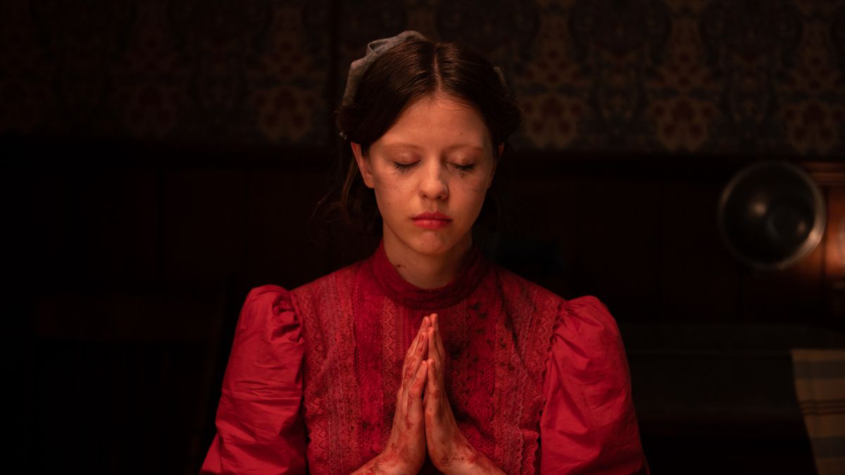 Mia Goth nei panni di Pearl in Ti West's Pearl, indossa un vestito rosso e con le mani giunte in preghiera