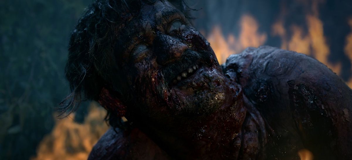 Un uomo con la pelle nera e carbonizzata, gli occhi pallidi e ciechi e i denti che si disintegrano alza lo sguardo verso la pioggia in una ripresa del film horror indiano Tumbbad