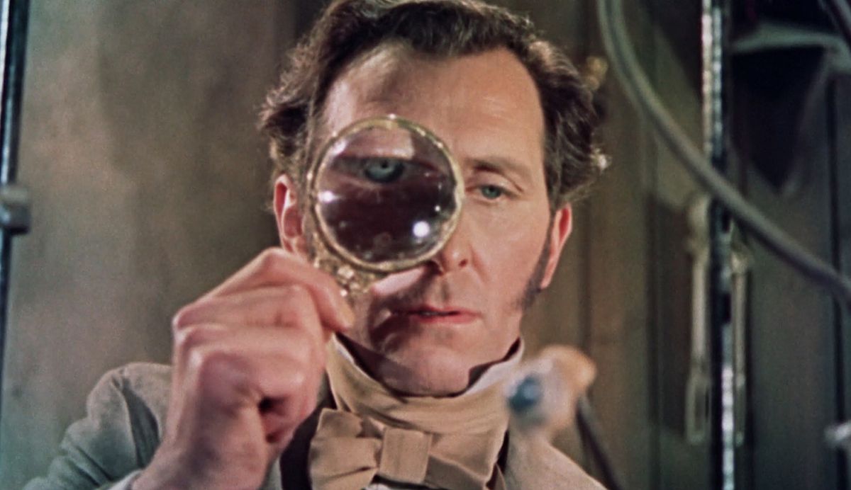 Peter Cushing nei panni del barone Frankenstein tiene una lente d'ingrandimento su un occhio nel suo laboratorio, facendo sembrare il suo viso distorto e ultraterreno, in La maledizione di Frankenstein del 1957