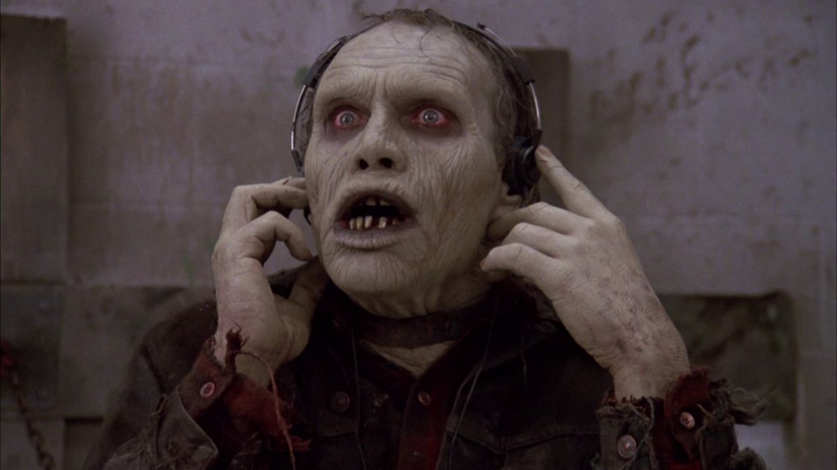 Uno zombi che indossa un collare dà uno sguardo di sorpresa mentre ascolta la musica con le cuffie over-ear in Il giorno dei morti di George Romero.