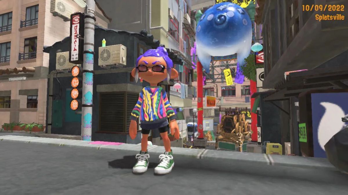 Un Octoling in Splatoon 3 che indossa un maglione multicolore, piccoli occhiali da sole e scarpe alte verdi.