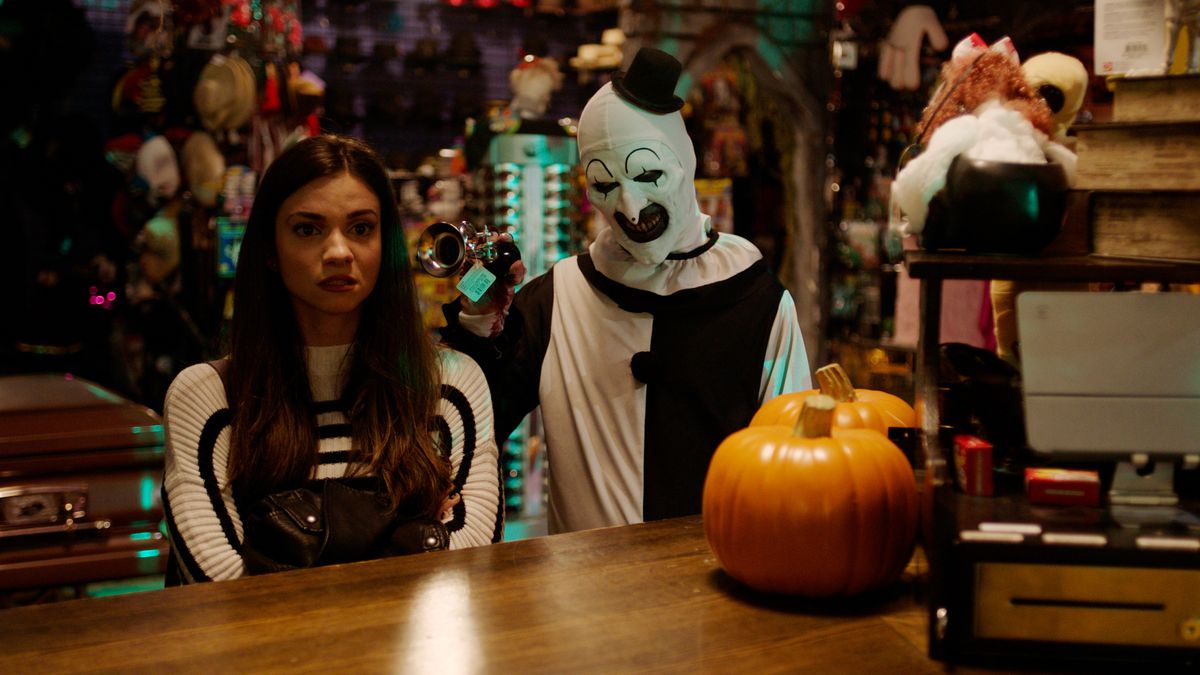 Lauren LaVera nei panni di Sienna Shaw è a disagio al bancone di un negozio di Halloween, guardando avanti mentre David Howard Thornton le suona un clacson d'argento nell'orecchio mentre il mimo assassino sorridente Art the Clown in Terrifier 2