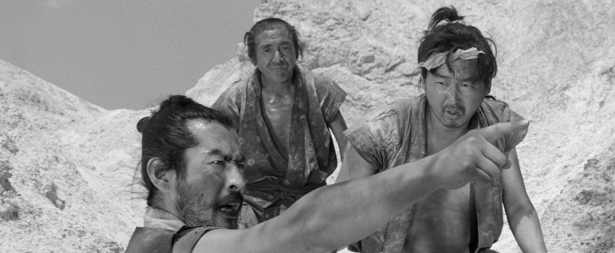 Tre uomini stanno sulla scogliera con uno di loro che indica e grida qualcosa fuori dallo schermo