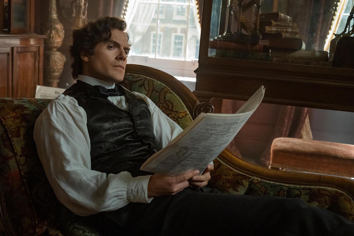 Henry Cavill nei panni di Sherlock Holmes.  si siede su una chaise longue, sbirciando alcune carte nelle sue mani