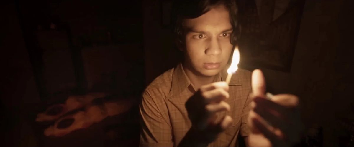 Un giovane tiene una candela in una stanza buia con due corpi avvolti in coperte sullo sfondo.