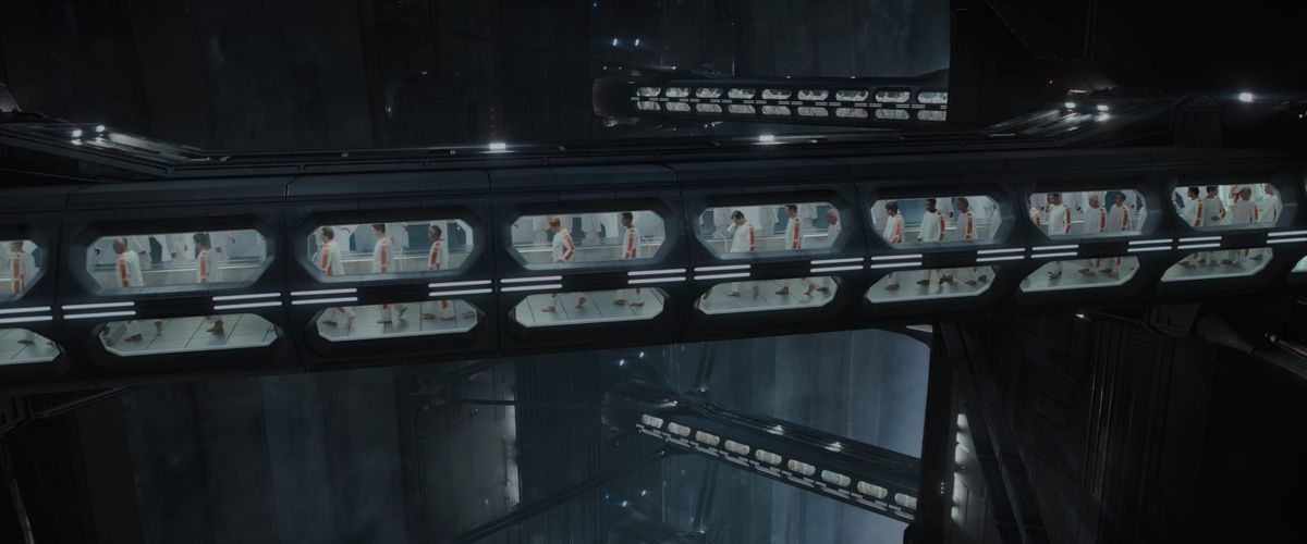 Prigionieri in tute bianche e arancioni visti camminare attraverso un corridoio di cavalcavia con cascate e altri cavalcavia dietro di loro ad Andor