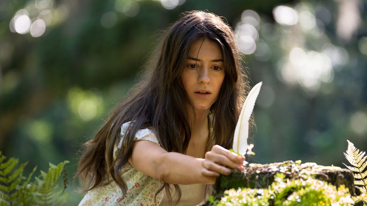 Una giovane donna con i capelli castani (Daisy Edgar-Jones) tiene una piuma contro un tronco illuminato dal sole con una foresta fuori fuoco sullo sfondo.