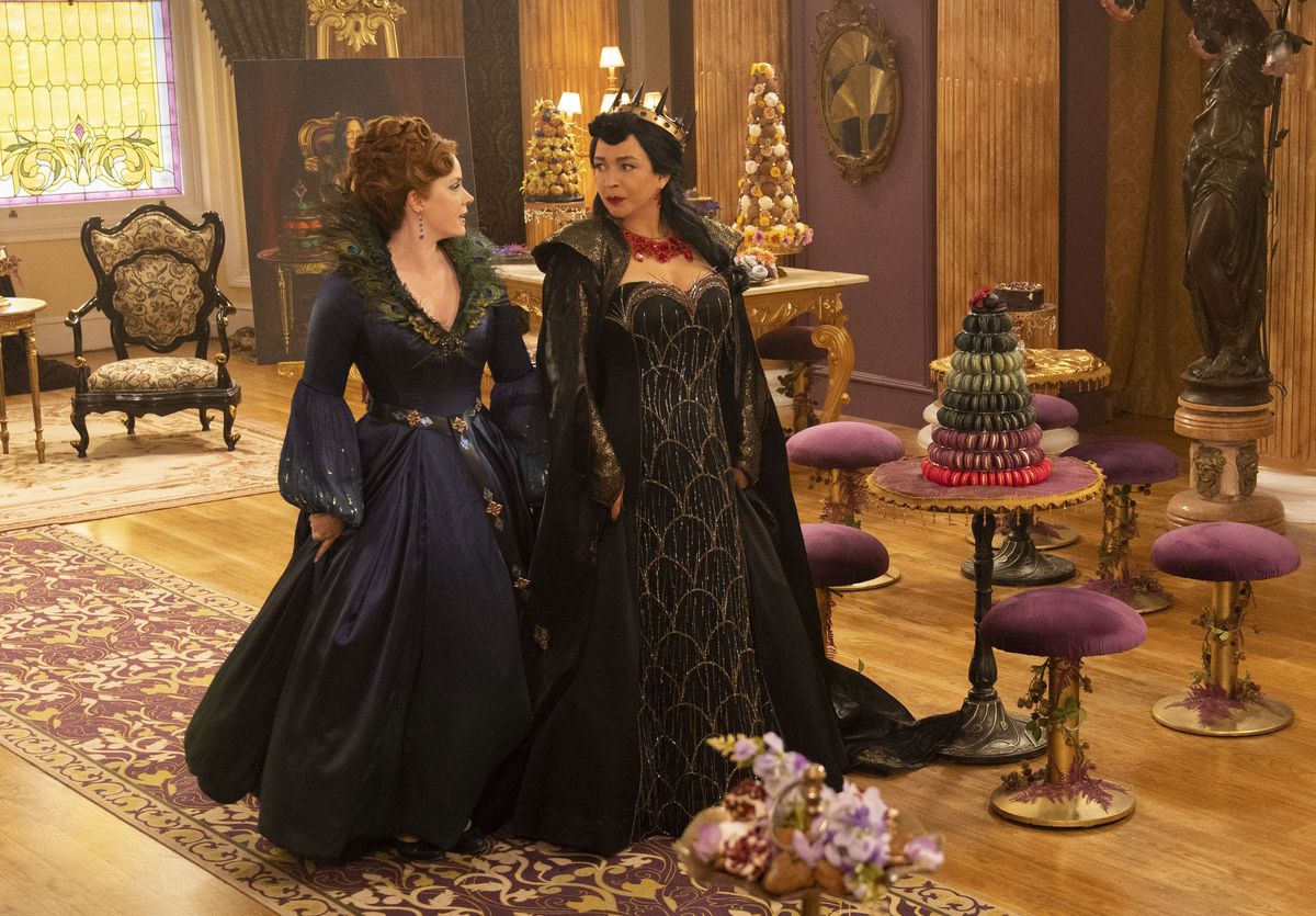 Giselle indossa un abito blu scuro e si trova spalla a spalla con la malvagia regina Malvina in una stanza decorata; entrambi si fissano l'un l'altro