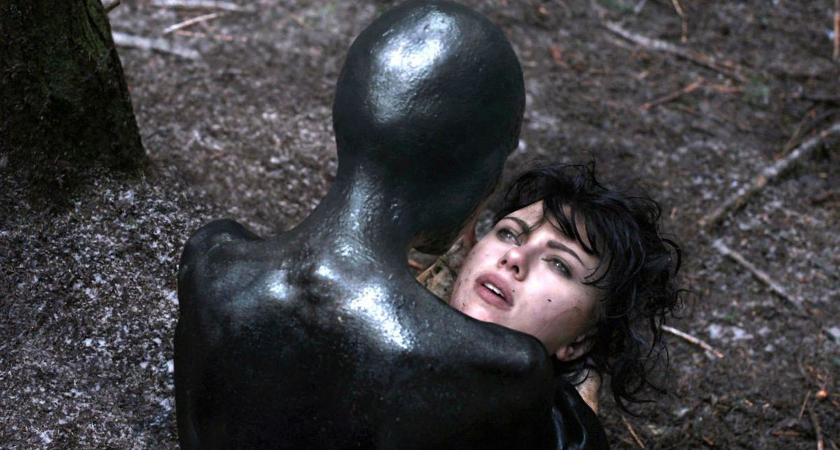 Una creatura umanoide nera tiene tra le mani un volto umano in Under the Skin.