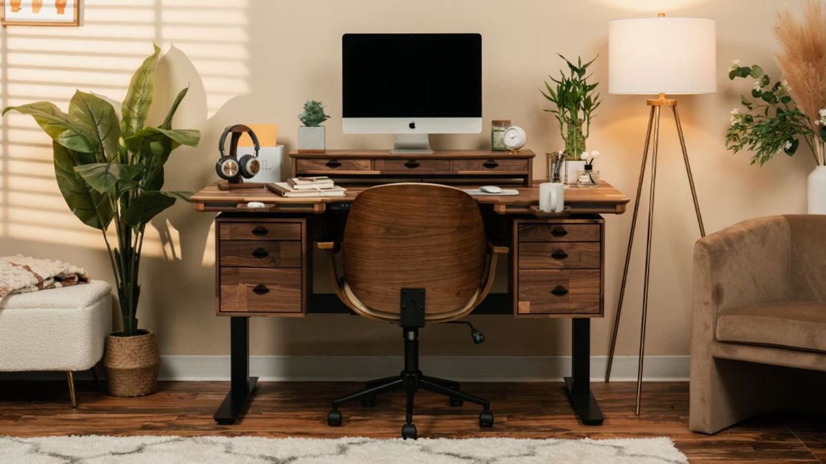 Al centro della scrivania modulare Wyrmwood c'è una cornice nera.  Il piano qui è in noce scuro, con due cubbies ciascuno con tre cassetti.  Un topper da scrivania contiene un monitor, mentre un accessorio magnetico contiene una tazza di caffè.