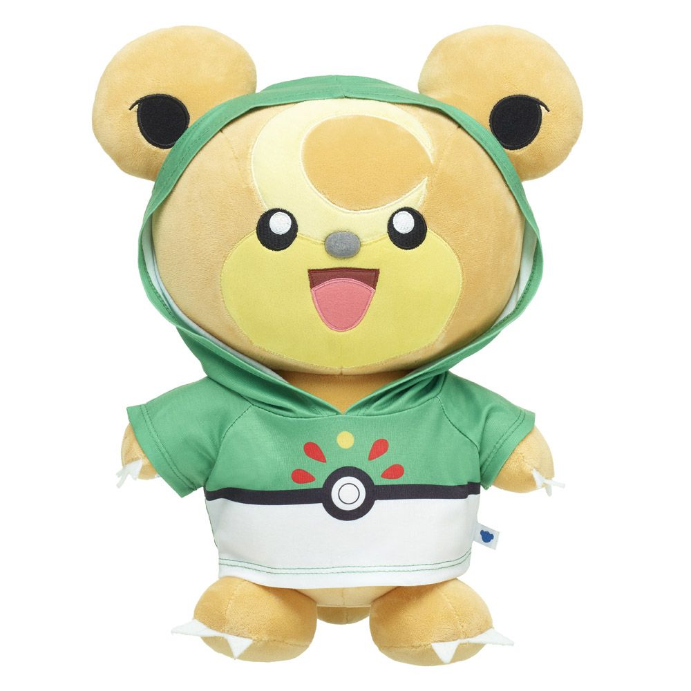 Un peluche di Teddiursa che indossa una felpa con cappuccio verde e bianca in stile come una Poké Ball su uno sfondo bianco.