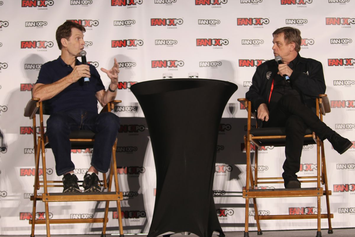 Kevin Conroy e Mark Hamill si siedono l'uno di fronte all'altro su un palco, chiacchierando.