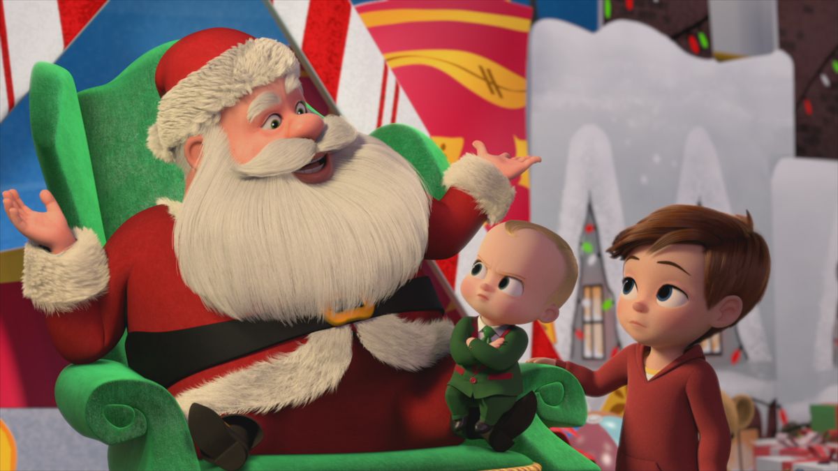 Un bambino dal viso severo in giacca e cravatta siede sulle ginocchia di Babbo Natale accanto a un ragazzo dall'aria preoccupata con un maglione con scollo a V.