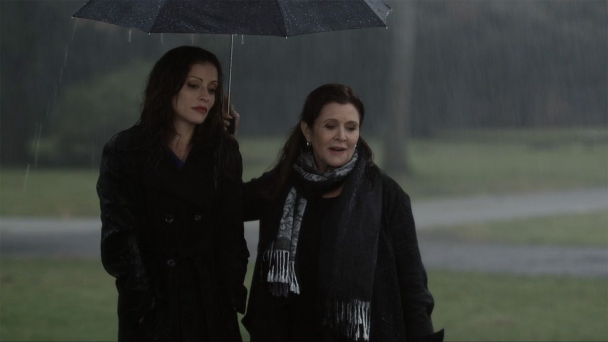 Carrie Fisher in nero tiene in mano un ombrello nero per coprire una donna bruna dalla pioggia in It's Christmas, Carol! (2012)