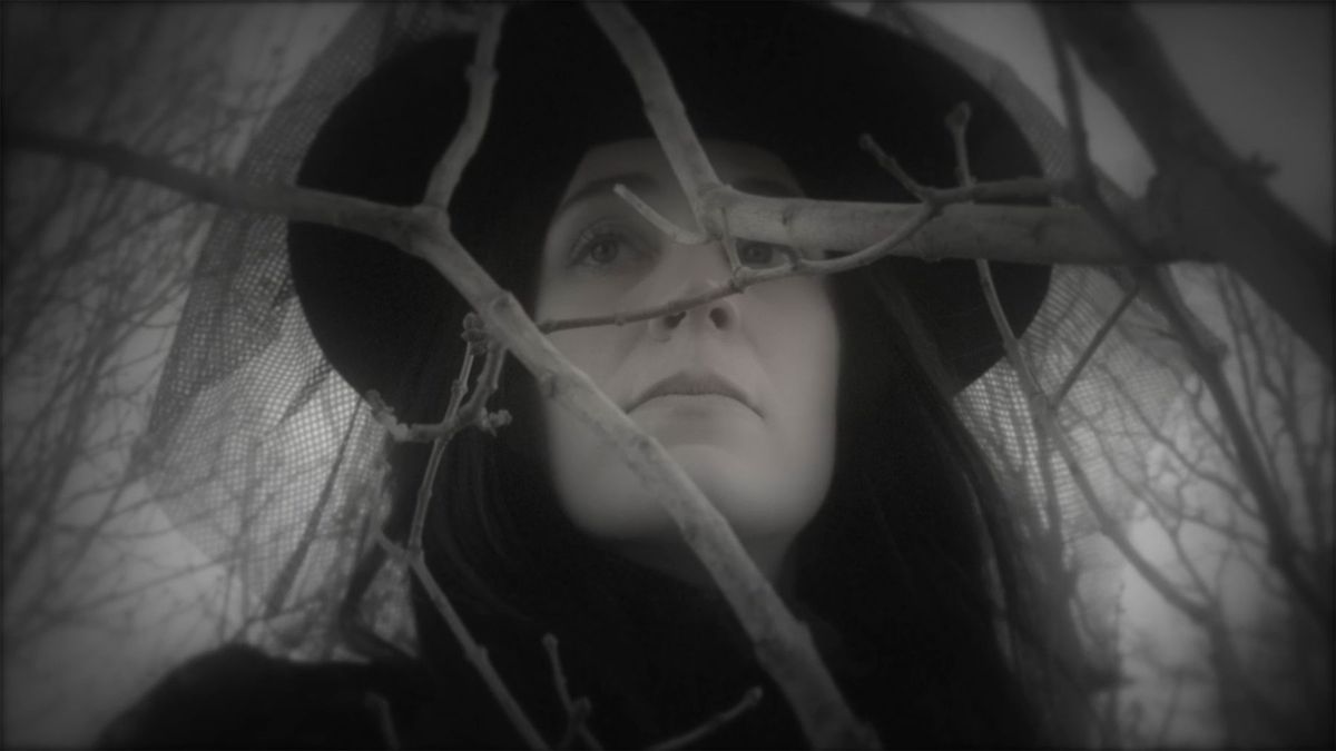 Una donna con un velo nero sta dietro un albero in A Christmas Carol (2015)