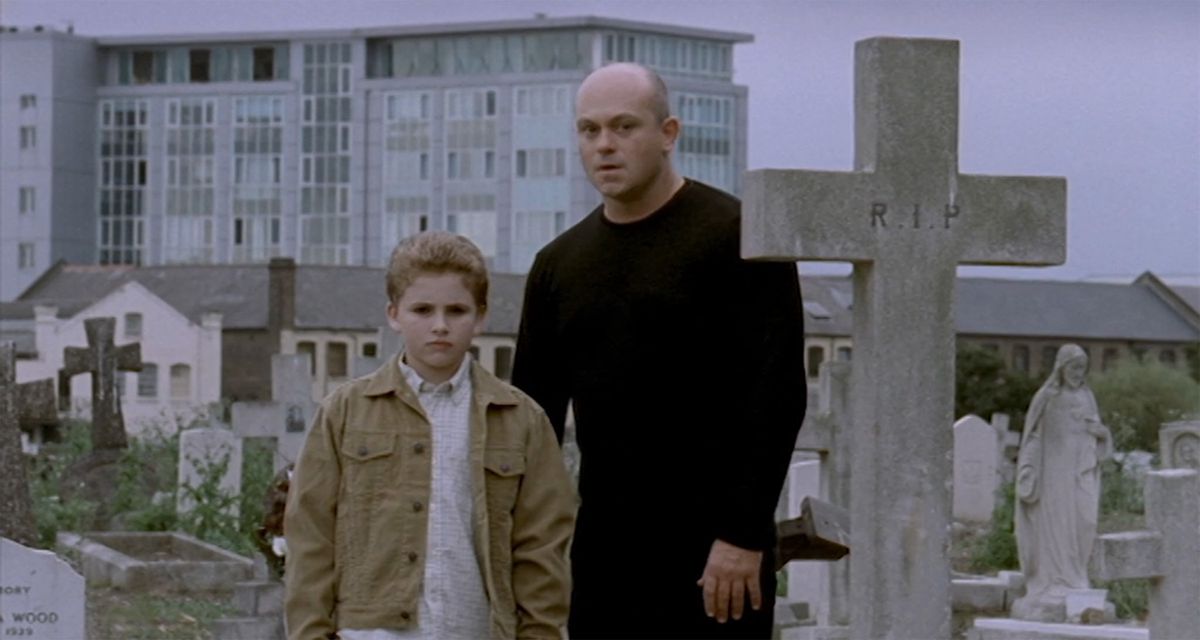 Un uomo calvo guida un bambino dai capelli rossi attraverso un cimitero in A Christmas Carol (2000)