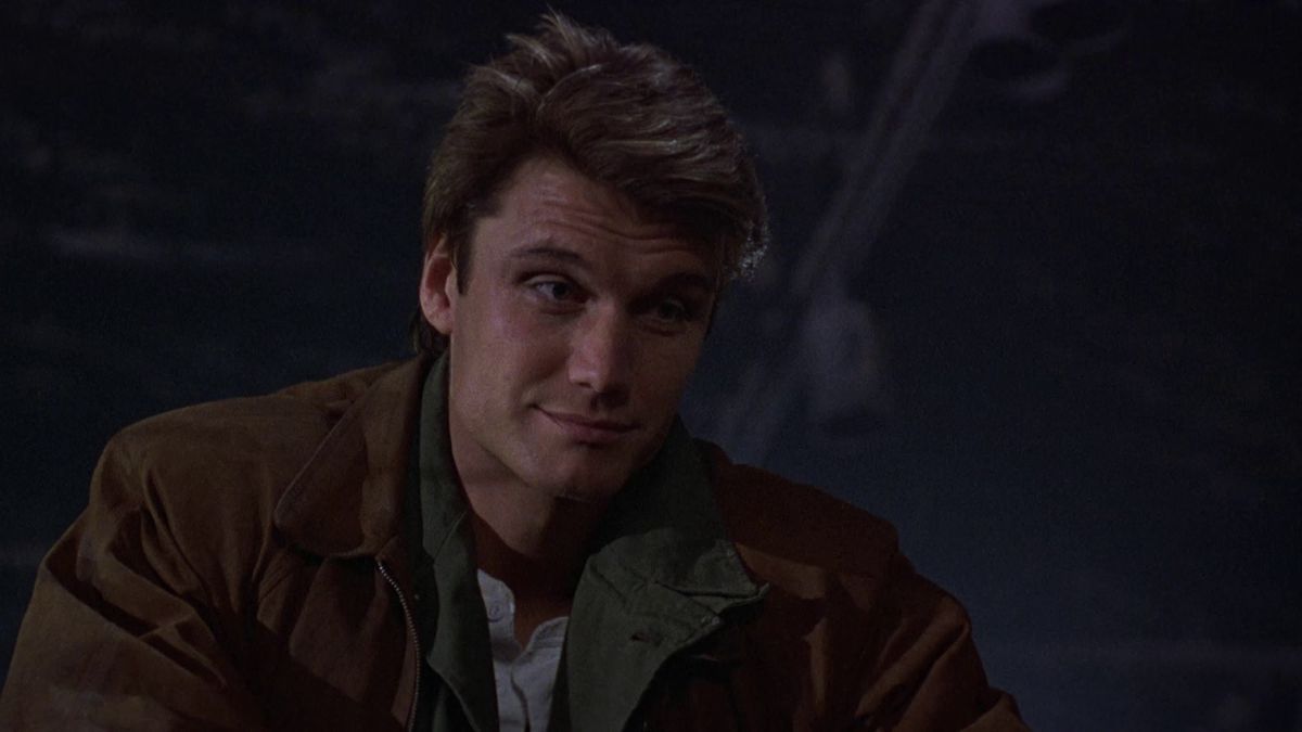 Dolph Lundgren è molto bello in Dark Angel, indossa un cappotto marrone e sorride leggermente.