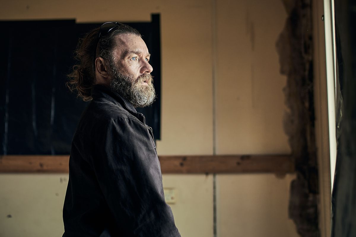 Joel Edgerton ha una barba estremamente folta mentre guarda fuori dalla finestra in The Stranger.