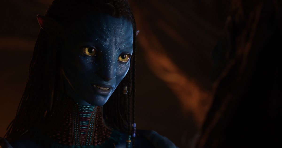 La protagonista di Na'vi Neytiri (Zoe Saldaña) siede in uno spazio buio e sorride a qualcuno fuori campo in una scena di Avatar: The Way of Water