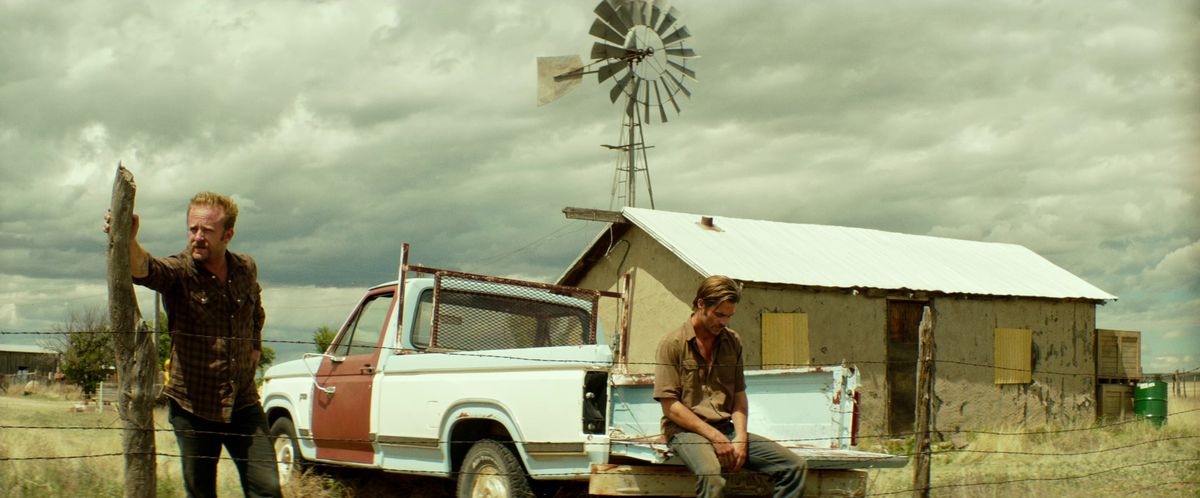 Chris Pine siede sul retro di un camioncino mentre Ben Foster si appoggia a un pezzo di legno in Hell or High Water.