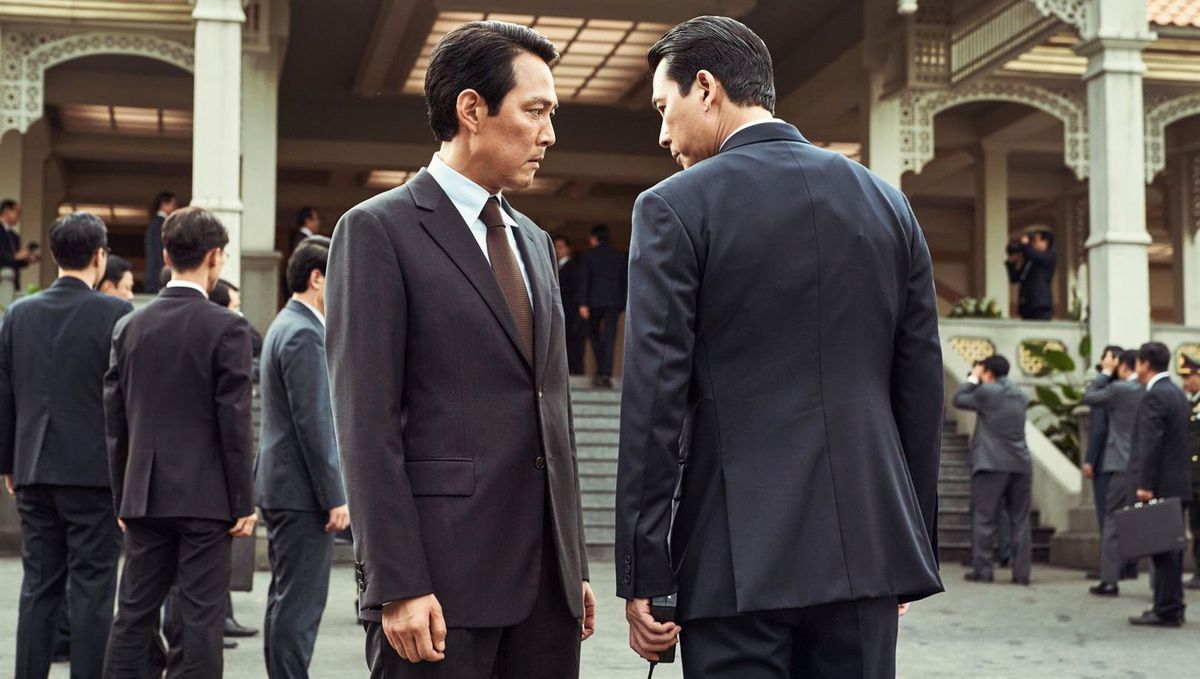 I capi rivali della KCIA Park (Lee Jung-jae) e Kim (Jung Woo-sung), entrambi con indosso abiti scuri, stanno uno di fronte all'altro e guardano torvo davanti a un edificio imponente circondato da altri agenti vestiti di scuro in Hunt