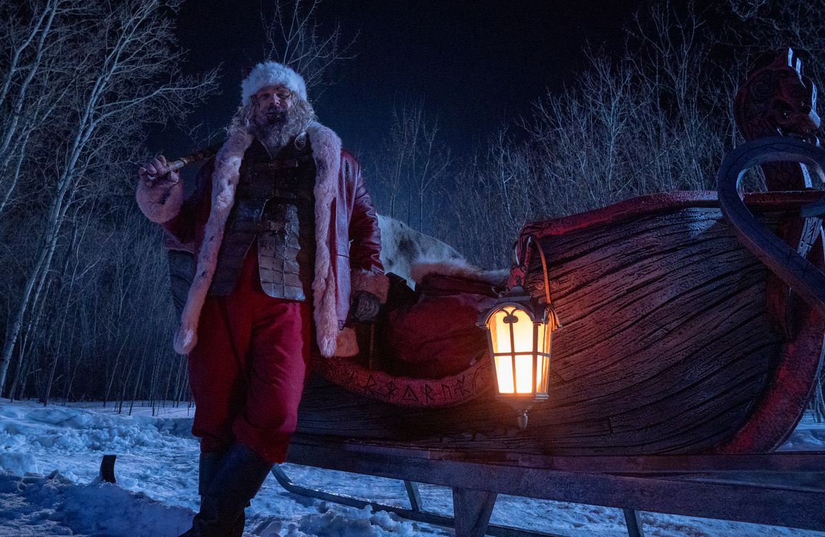 Babbo Natale (David Harbour) si appoggia ubriaco alla sua slitta, un veicolo a forma di barca di legno rosso sangue scolpito con rune nordiche, in Violent Night