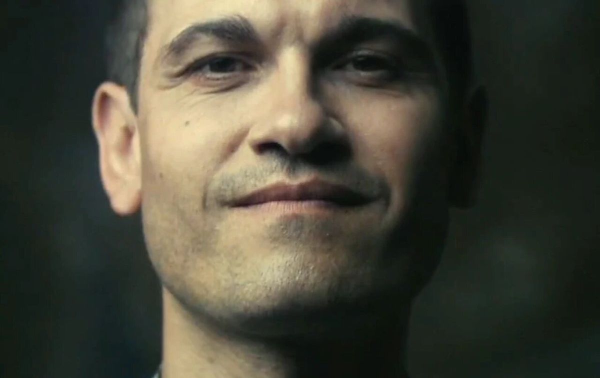 Un uomo dai capelli neri tagliati corti (Frédéric Bourdin) che guarda avanti e sorride.