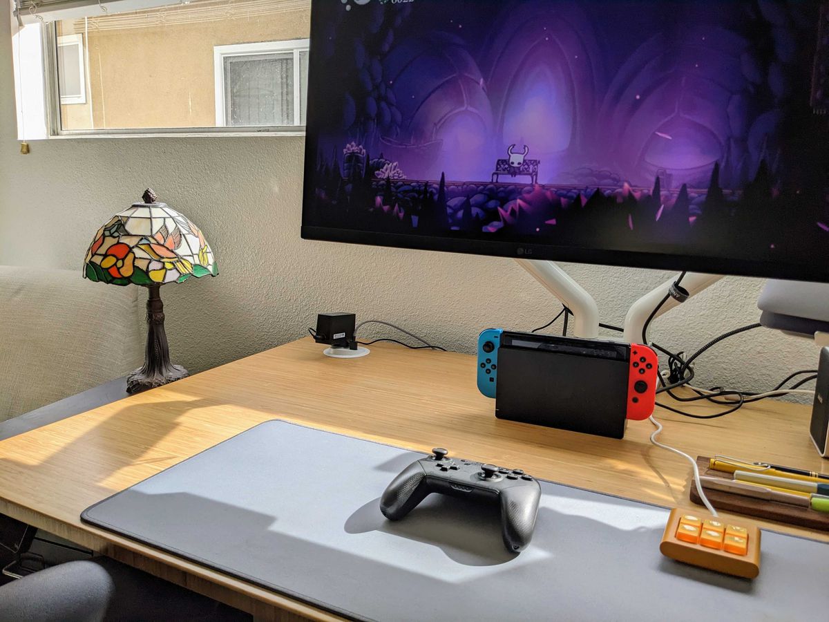 Una configurazione da scrivania con un Nintendo Switch e un grande monitor da gioco, con un controller Nintendo Switch pro su un tappetino da scrivania.