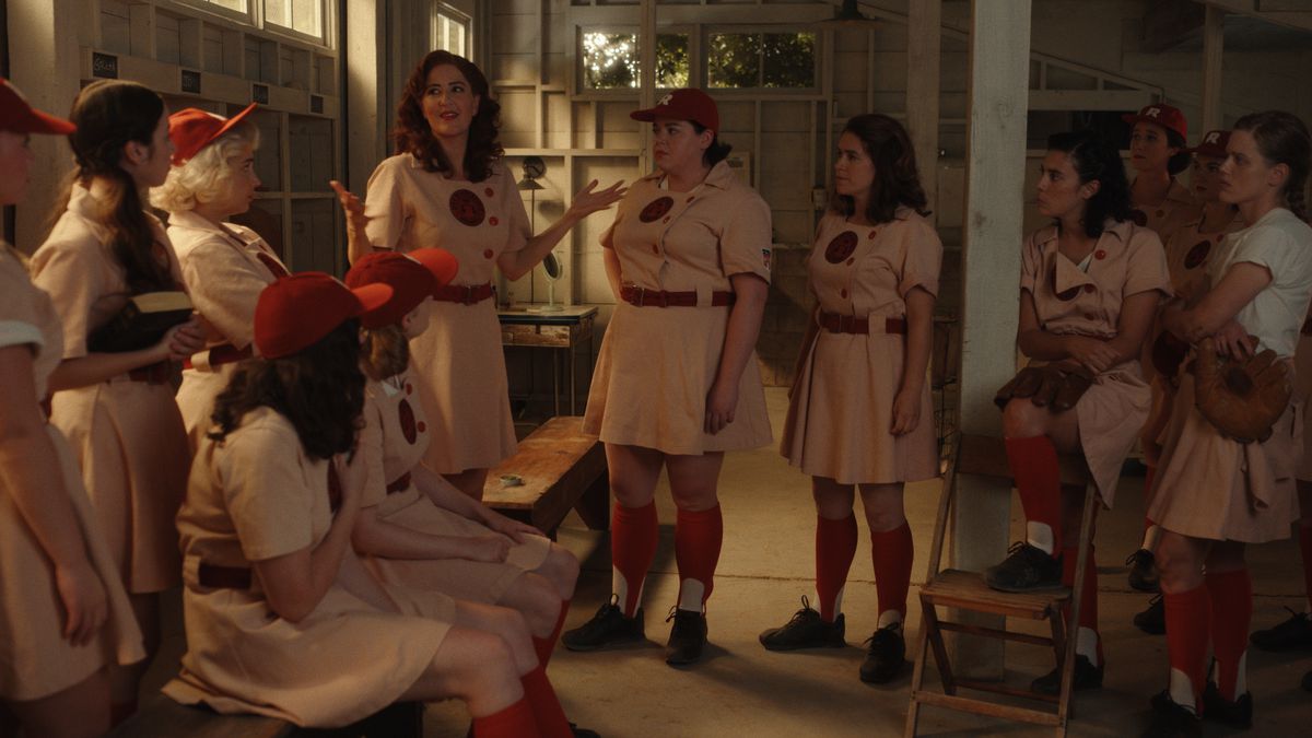 Greta (D'Arcy Carden) in piedi e parla con la squadra dei Rockford Peaches riunita negli spogliatoi