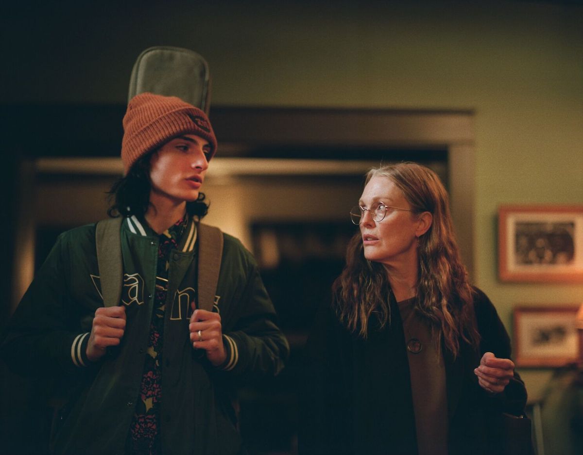 Un adolescente (Finn Wolfhard) con una custodia di chitarra sulla schiena è in piedi accanto a una donna anziana dai capelli lunghi (Julianne Moore) con gli occhiali.