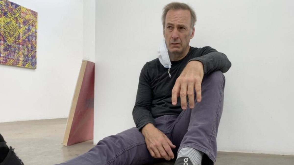 Un uomo dall'aspetto smunto (Bob Odenkirk) si accasciò sul pavimento contro il muro bianco e spoglio di una galleria d'arte.
